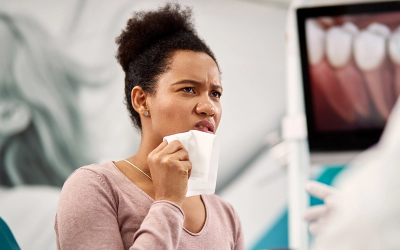 Woman holding tissue with concerned expression in dental office examining room.