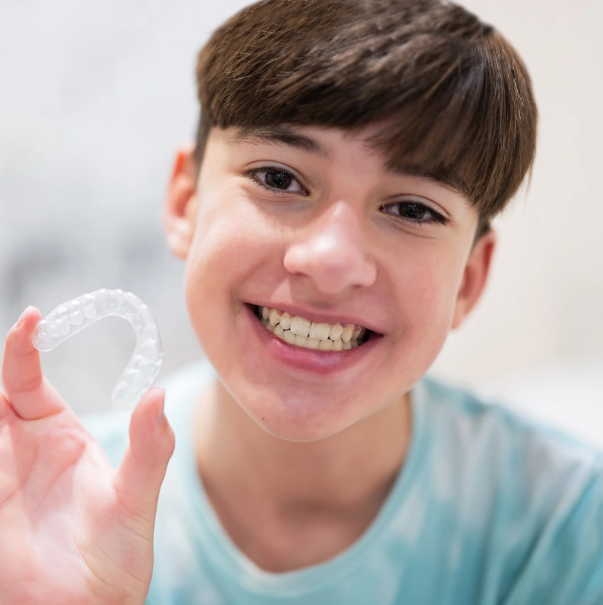 Teen smiling while holding Invisalign clear aligners