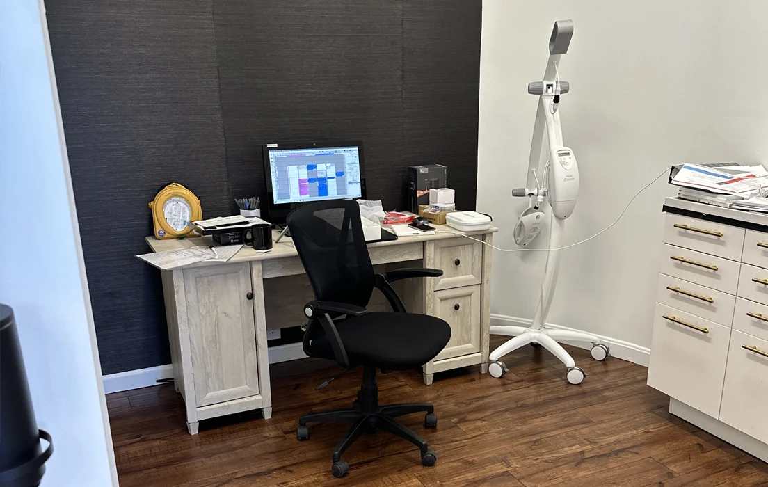 Modern dental office workspace with computer monitor, ergonomic chair, and professional equipment on wooden desk.
