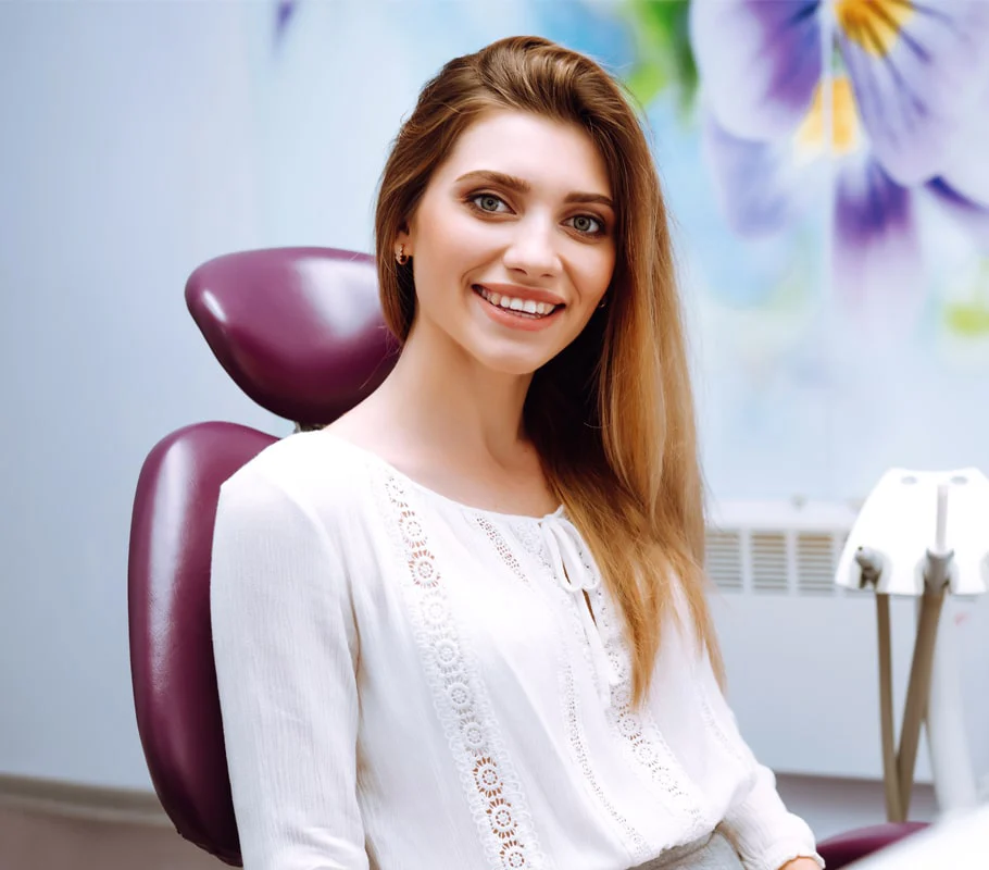 Smiling woman in dental chair wearing white blouse in modern dentist office.